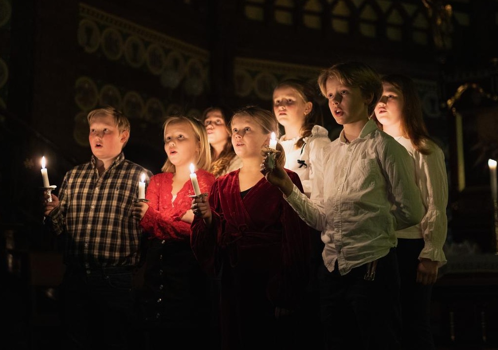 Syv barn som står i mørket med levende lys og synger