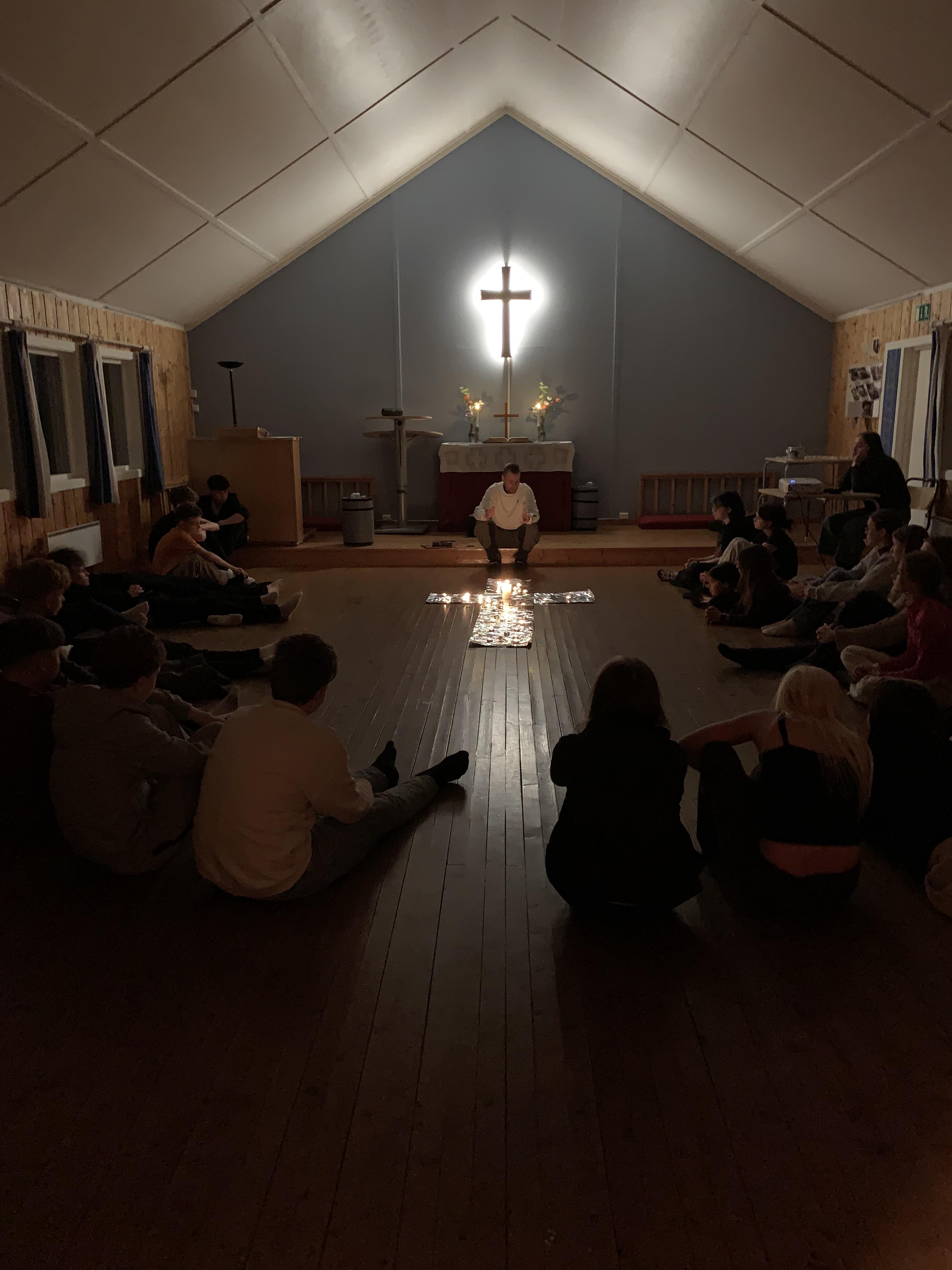 Bilde av 30 ungdommer som sitter rundt korset for kveldssamling